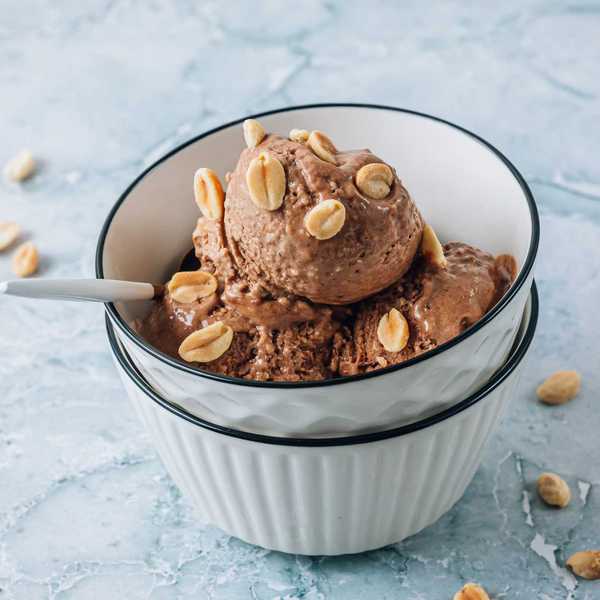 Chocolate ice cream with peanuts in a white bowl, placed on a light marble surface.