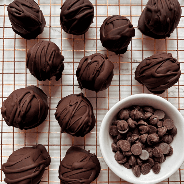 Chocolate truffles on a cooling rack with a bowl of chocolate chips.