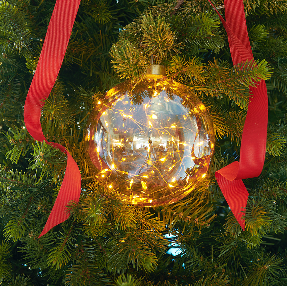 Clear glass ornament with lights on a Christmas tree, adorned with a red ribbon.