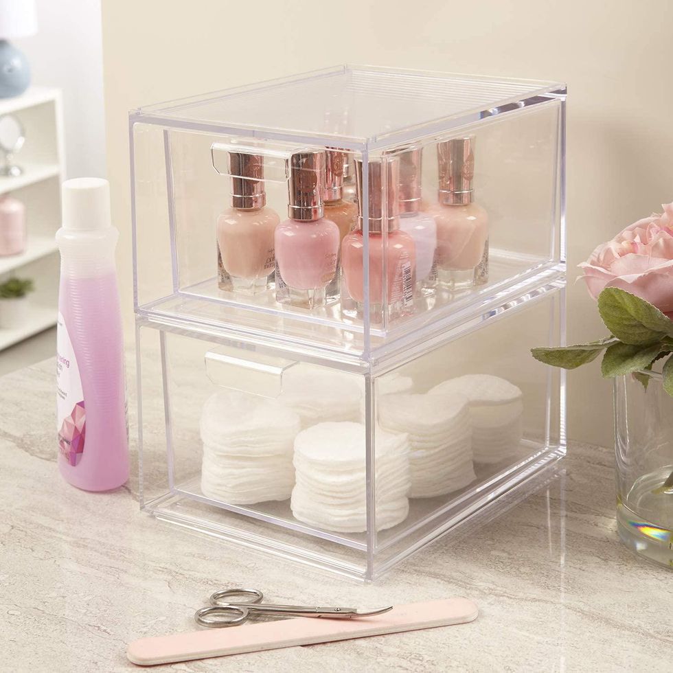 Clear organizer with nail polish and cotton pads on a bathroom counter.