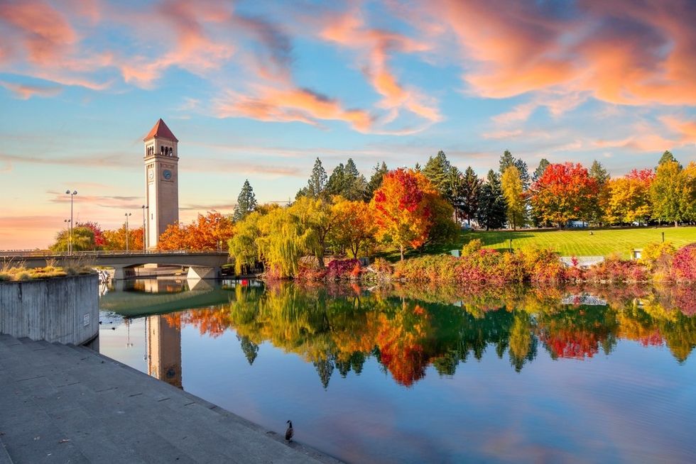 Clock tower and autumn trees reflected in a calm river under a colorful sky.