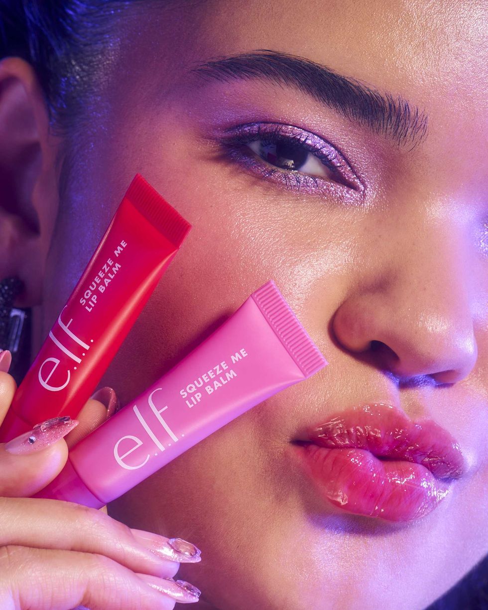 Close-up of a person with glossy lips holding e.l.f. lip balms in pink and red tubes.