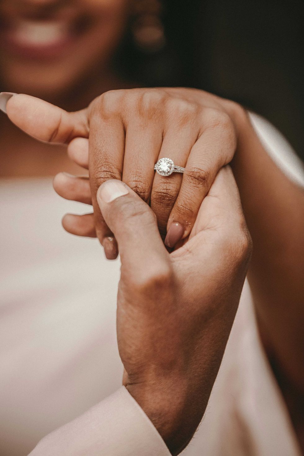 Close-up of hands with an engagement ring, person smiling in the background.