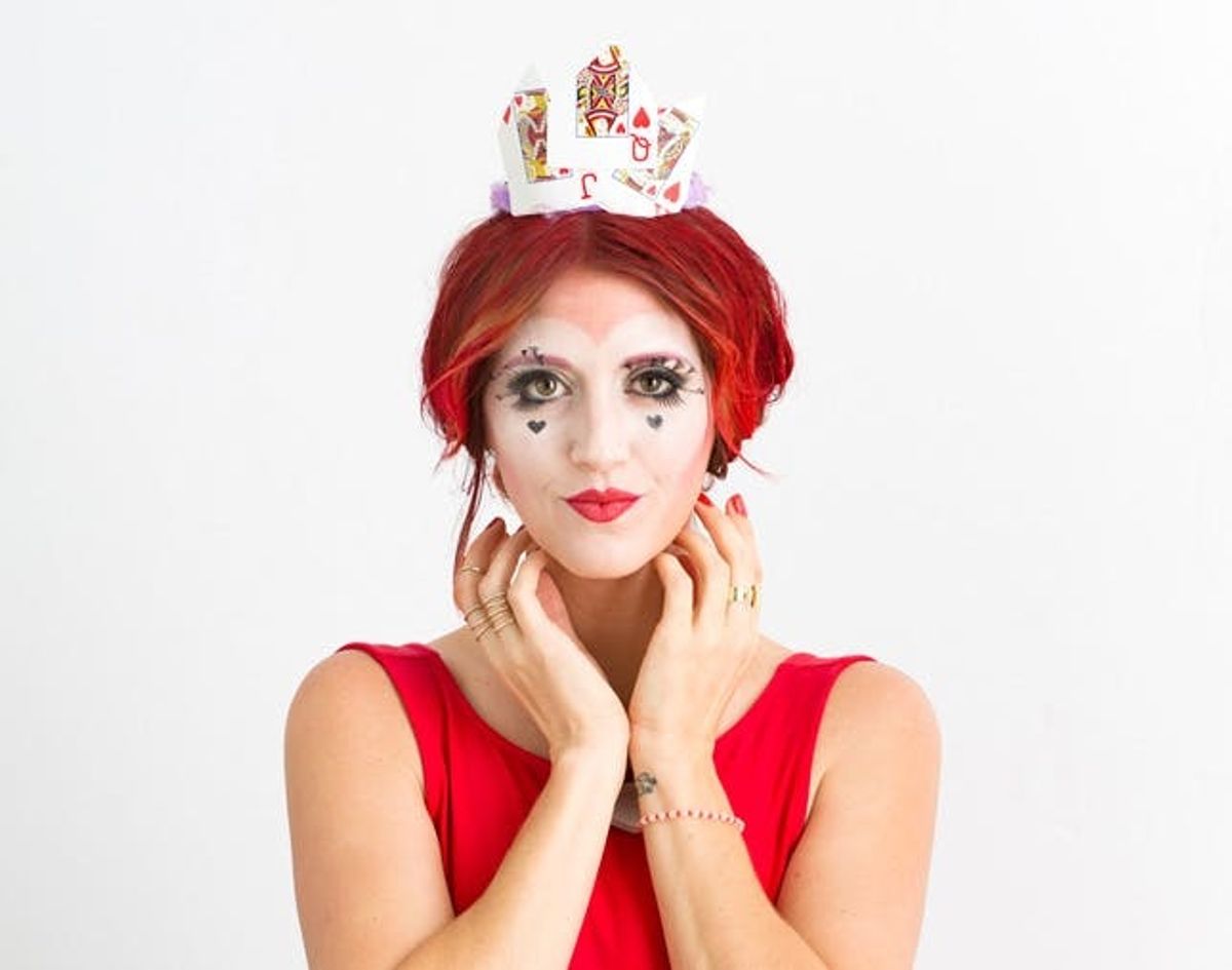 Close up of seated women in red dress with red hair showing off the classic Queen of Hearts makeup and costume.
