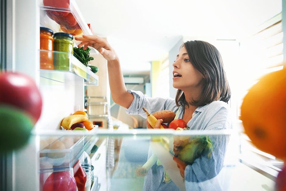 Closeup of a young woman picking some fruit and veggies from the fridge to make some healthy breakfast on Sunday morning. Shot from inside the working fridge.