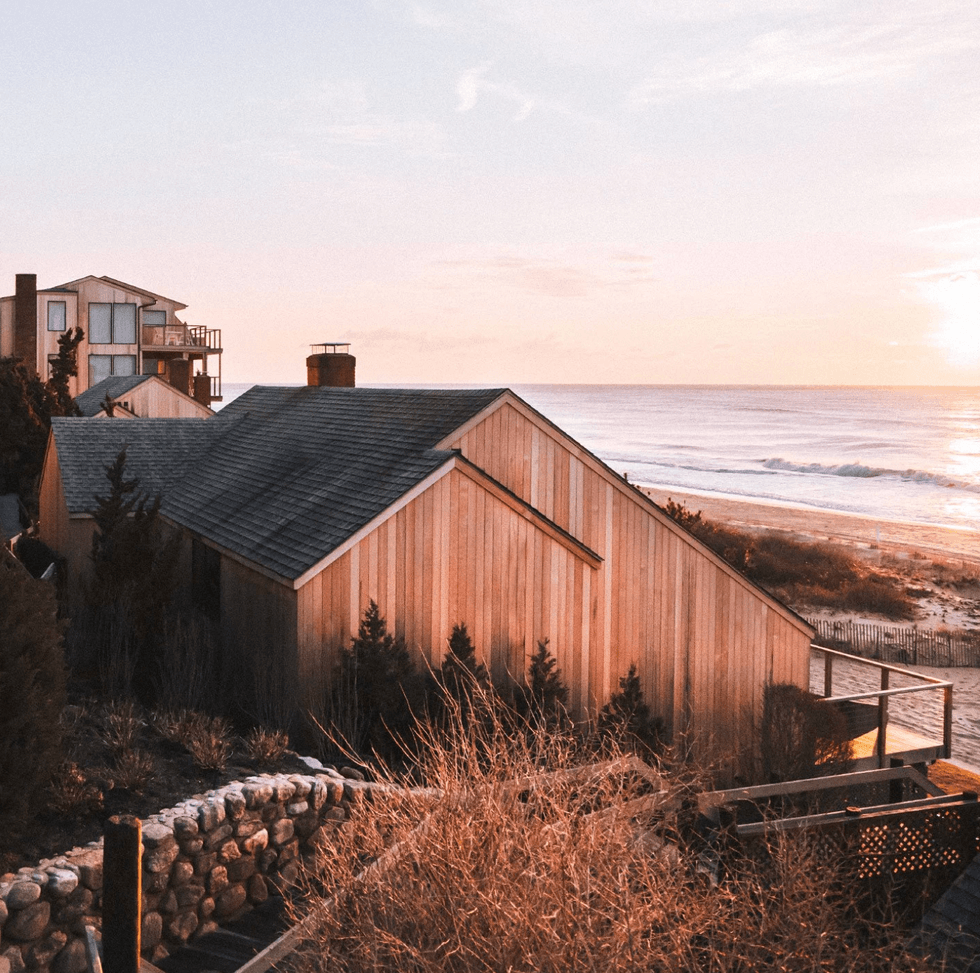 Coastal houses overlooking a serene ocean during a pastel-hued sunset.