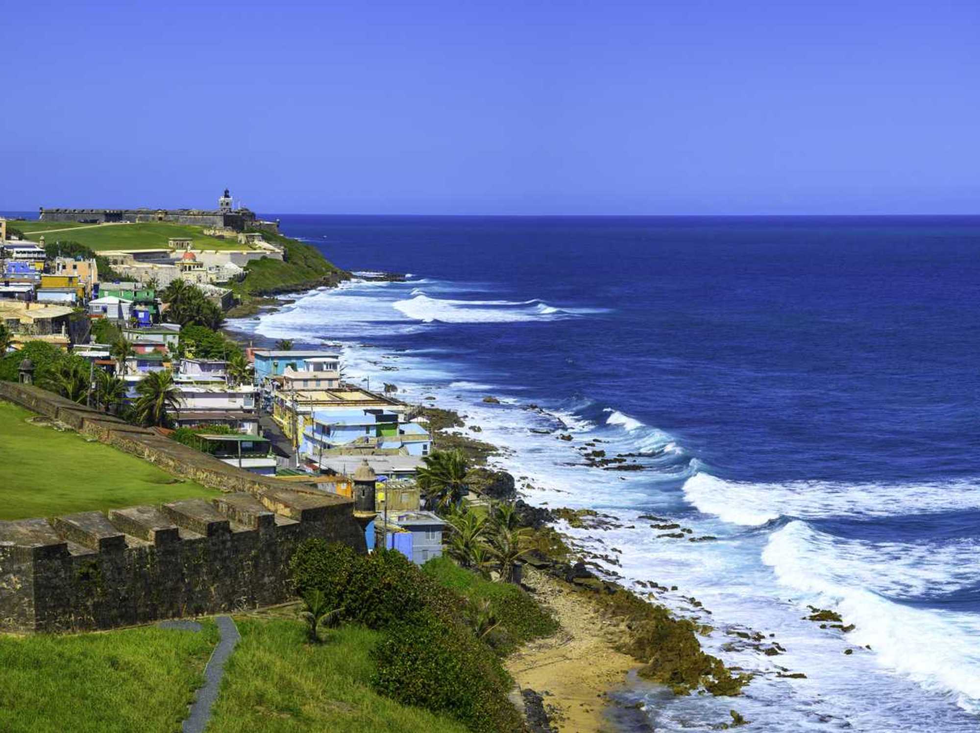 Coastal view of colorful buildings and waves by a historic fort in San Juan, Puerto Rico.