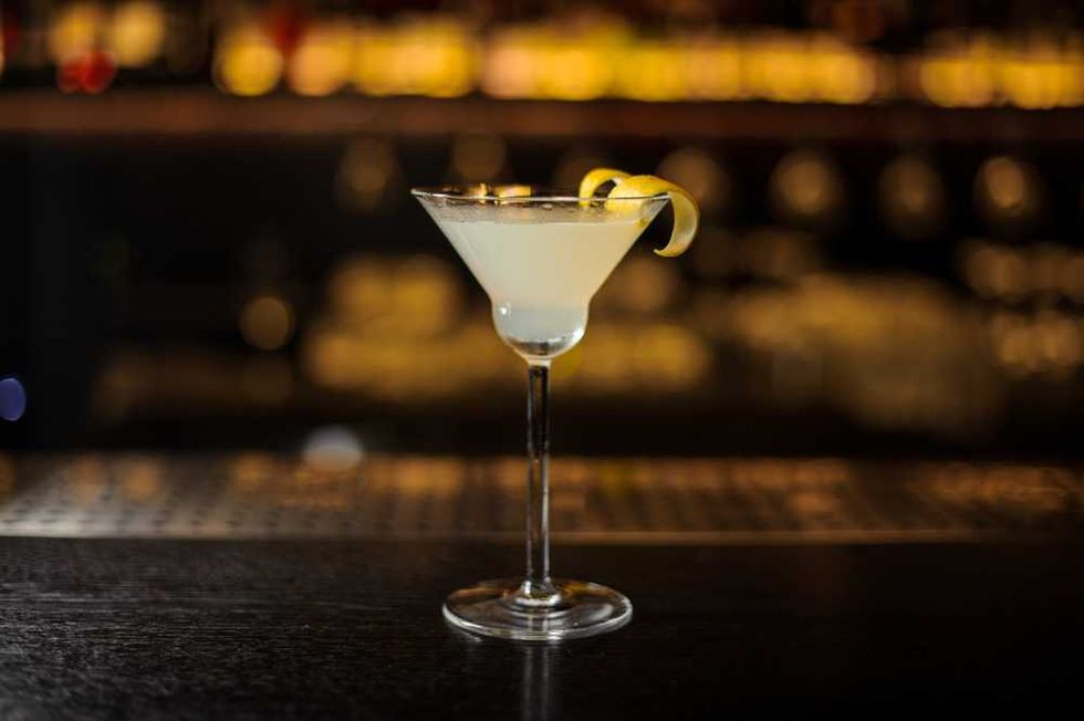 Cocktail glass with lemon twist garnish on a dimly lit bar counter.