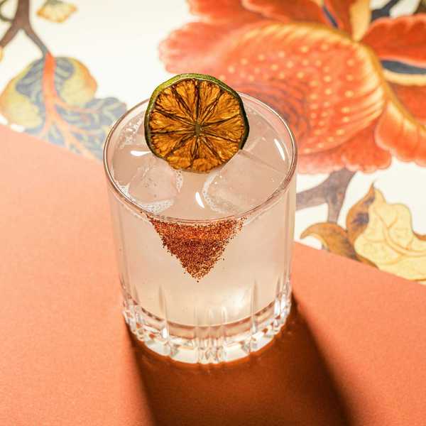 Cocktail with dried lime garnish and spiced rim on decorative background.