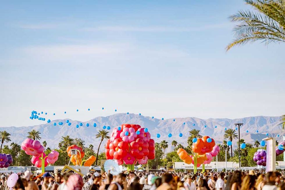 Colorful balloons and crowd at a festival, with mountains and palm trees in the background.