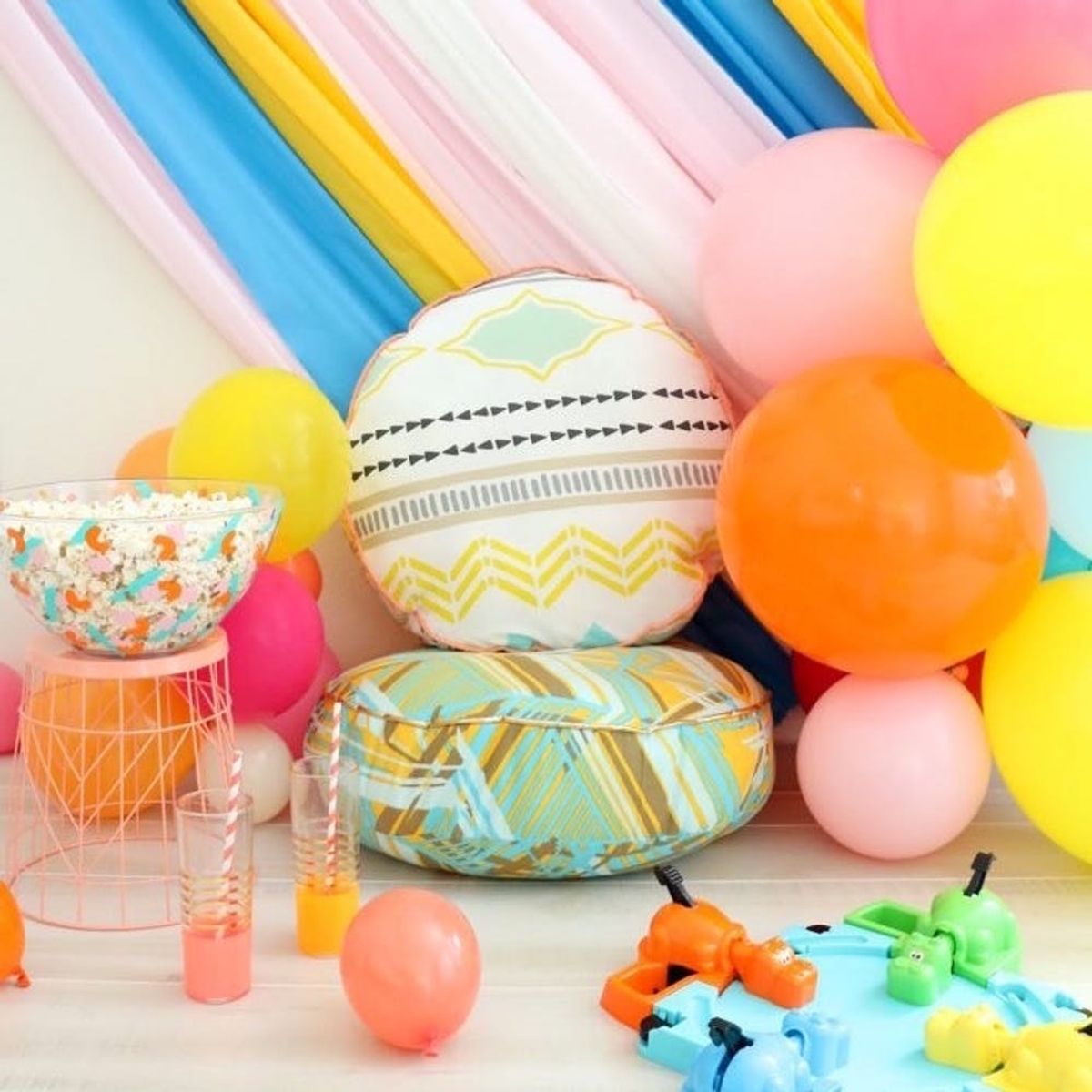 Colorful balloons, pillows, toy hippos, and popcorn in a bowl create a festive party setting.