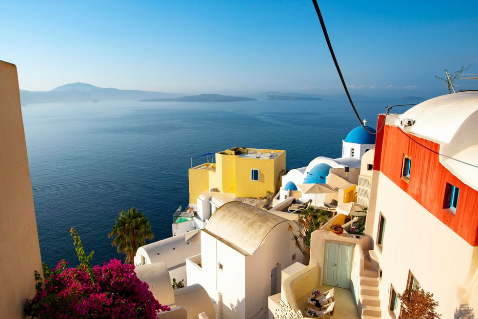 Colorful buildings overlook a serene blue sea with distant islands and clear skies.