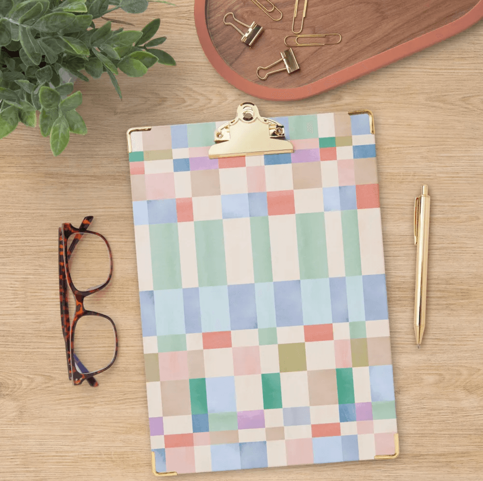 Colorful clipboard on desk with glasses, pen, plant, and paperclips.