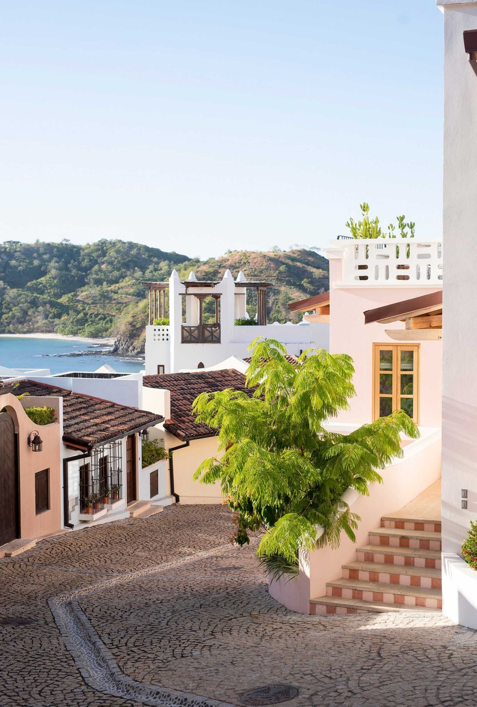 Colorful coastal village with cobblestone streets and lush greenery against ocean backdrop.