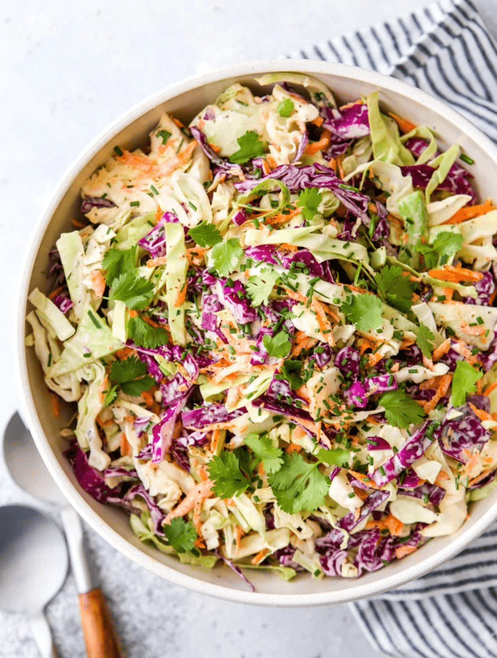 Colorful coleslaw with herbs in a bowl on a striped cloth.