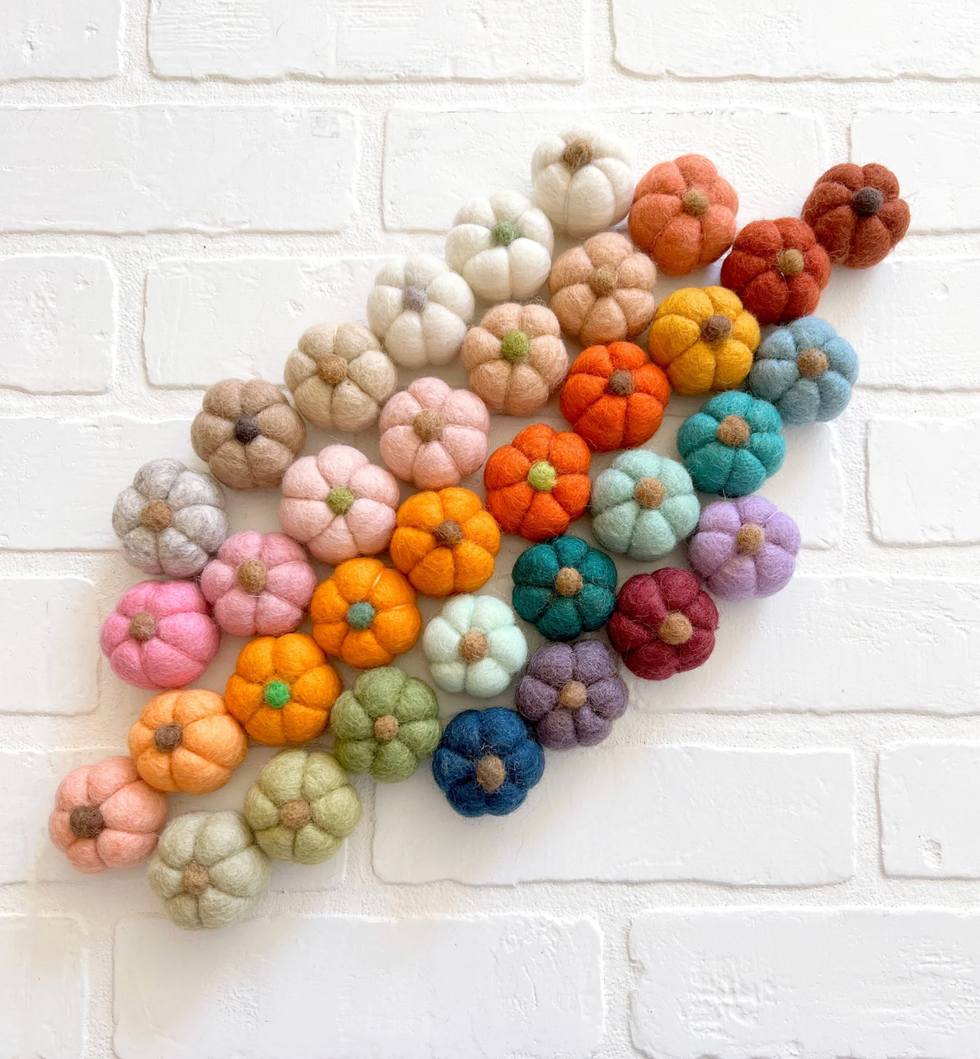 Colorful felt pumpkins arranged in rows on a white brick background.