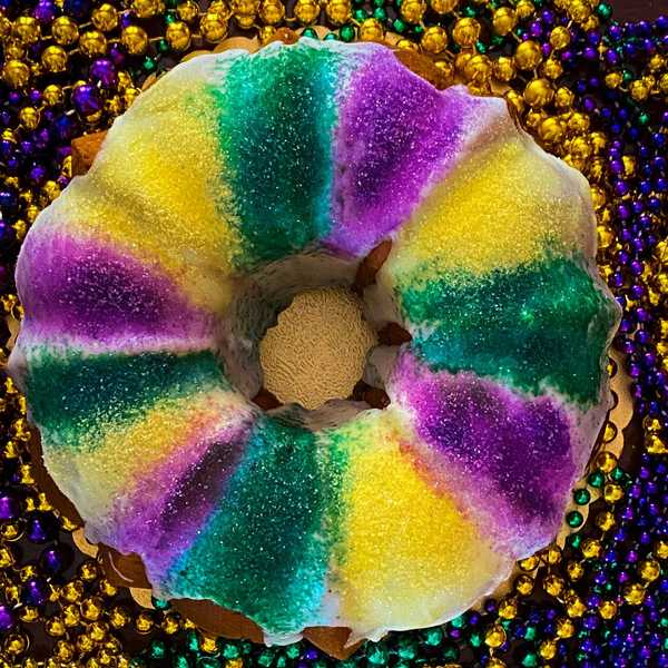 Colorful king cake with purple, green, yellow sugar, surrounded by Mardi Gras beads.