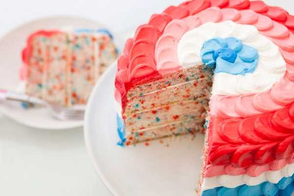 Colorful layered cake with red, white, and blue frosting and confetti interior.