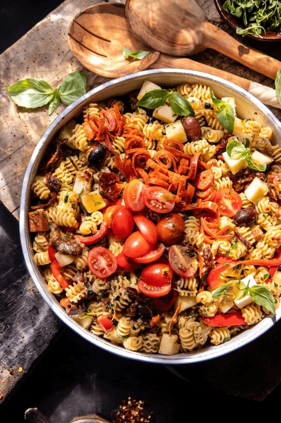 Colorful pasta salad with cherry tomatoes, olives, cheese, and basil in a bowl.