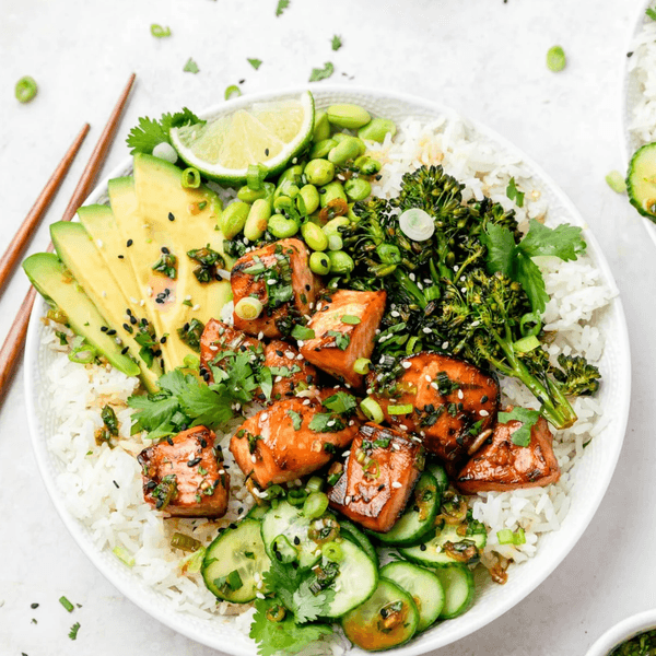 Colorful poke bowl with salmon, avocado, rice, edamame, greens, and cucumber slices.