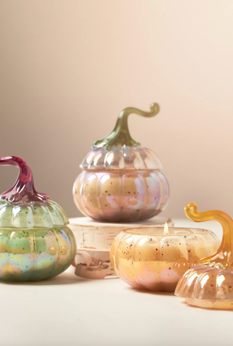 Colorful pumpkin-shaped candles, one lit, on a light background.