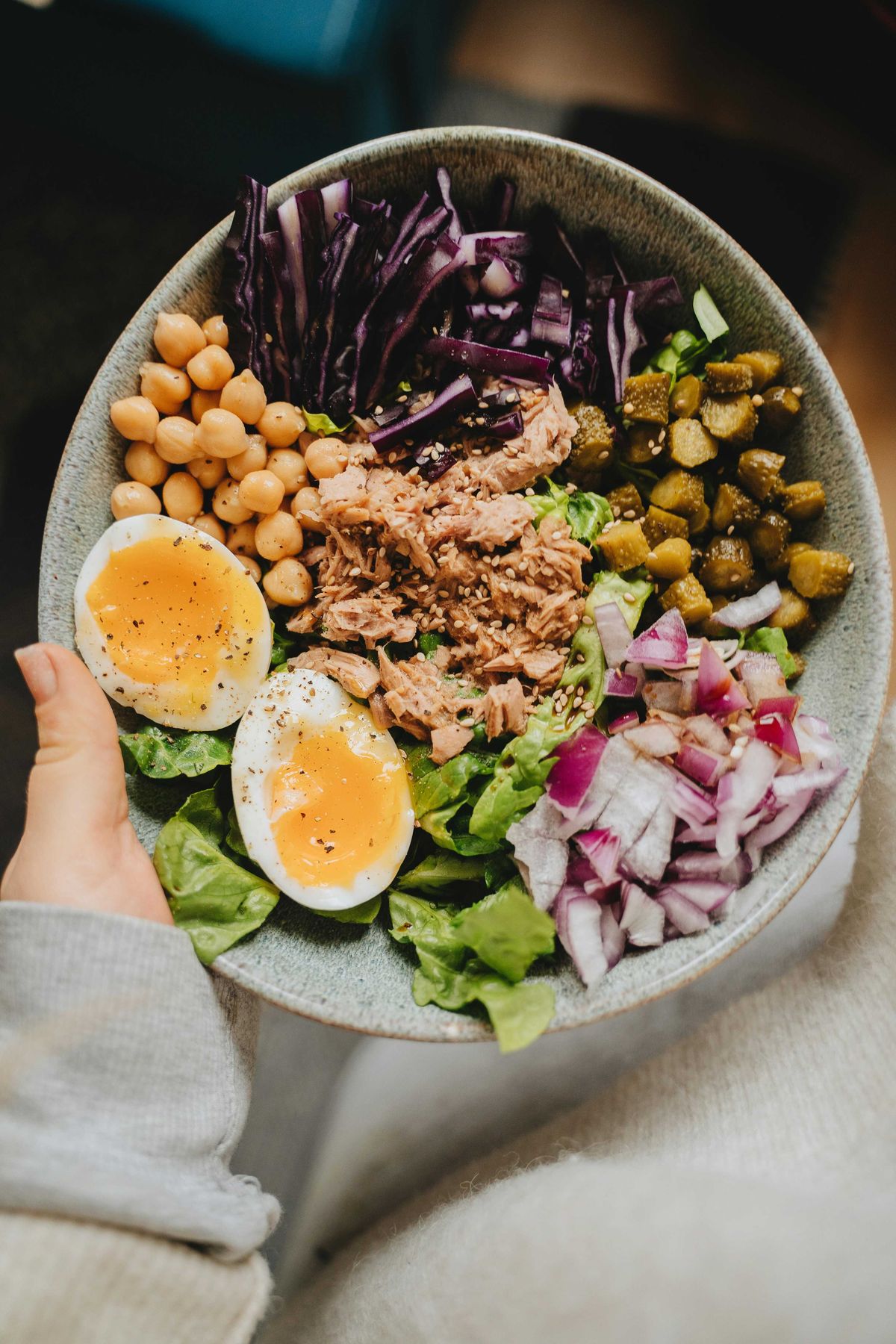 Colorful salad bowl with eggs, tuna, chickpeas, red cabbage, pickles, and onions.