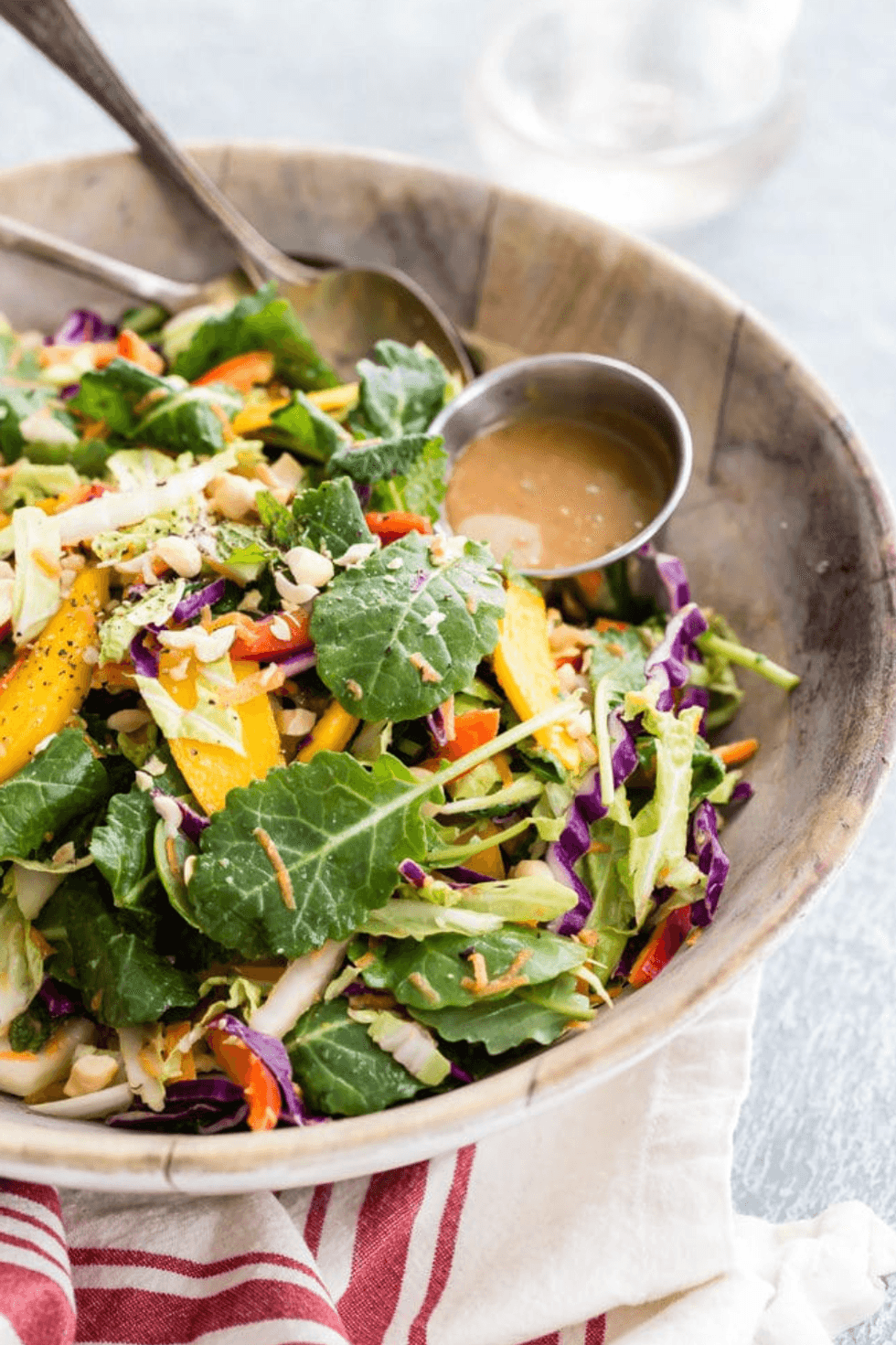 Colorful salad in a wooden bowl with dressing on the side.