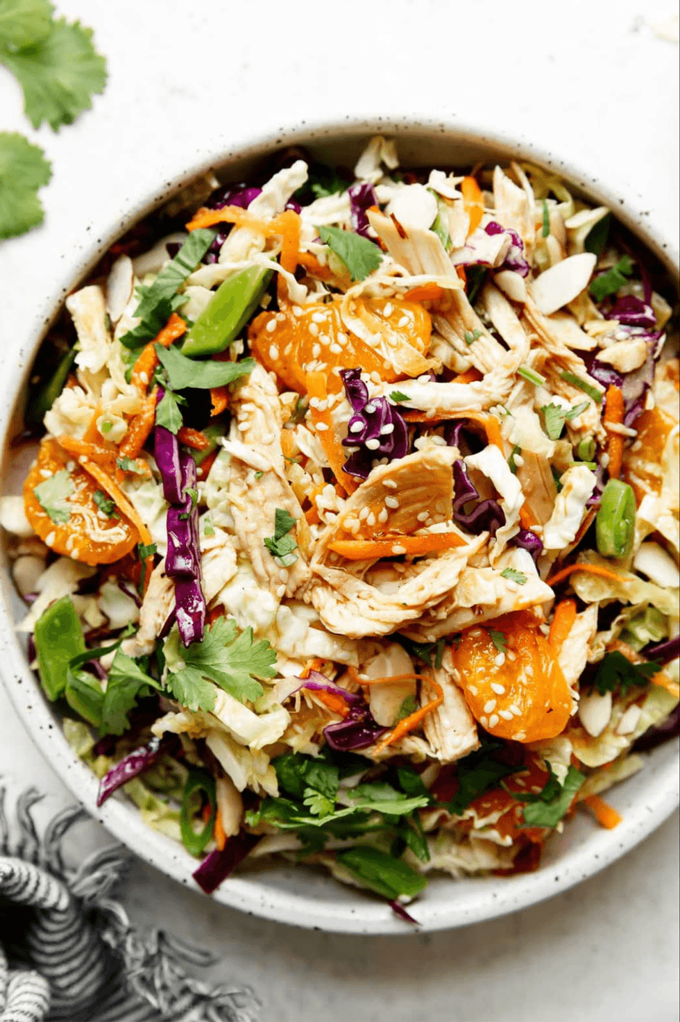 Colorful salad with cabbage, chicken, oranges, almonds, and cilantro in a white bowl.
