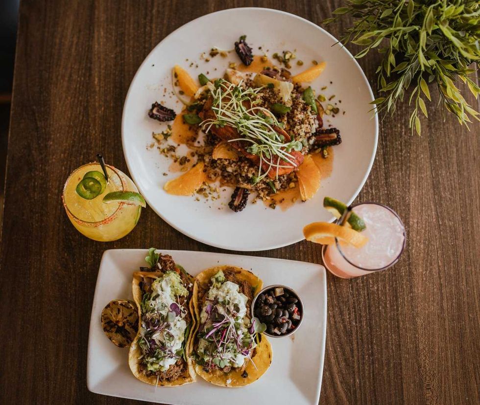 Colorful tacos, quinoa salad, and two cocktails on a wooden table, garnished elegantly.