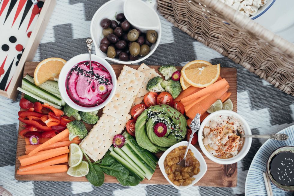 Colorful vegetable platter with dips, crackers, and garnishes on a picnic blanket.