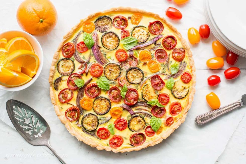 Colorful vegetable tart with tomatoes, zucchini, and basil next to sliced oranges.