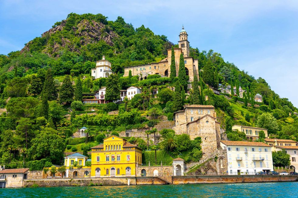 Colorful villas and lush greenery on a hillside by the water, under a clear blue sky.