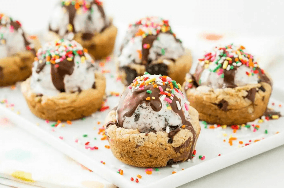 Cookie cups with ice cream, chocolate drizzle, and sprinkles on a white tray.