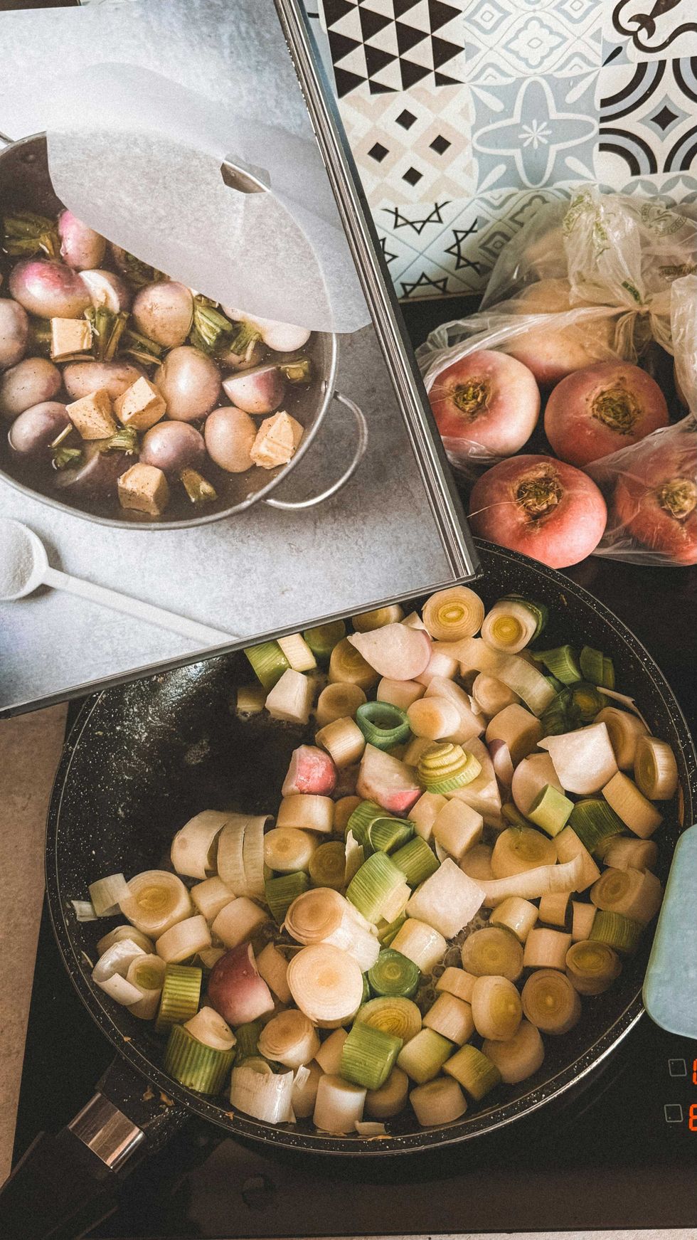 Cooking leeks and turnips in a pan with recipe book and raw turnips in view.