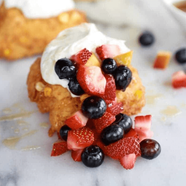 Corn fritter topped with whipped cream, blueberries, and strawberries.