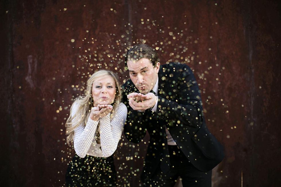 couple dressed in black and white blows gold glitter toward the camera