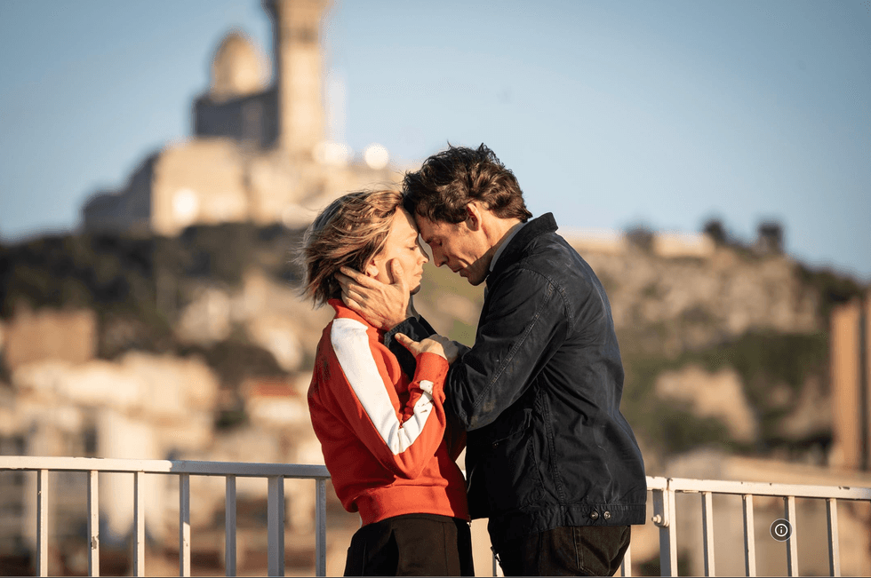 Couple embracing closely on rooftop with blurred cityscape in background.