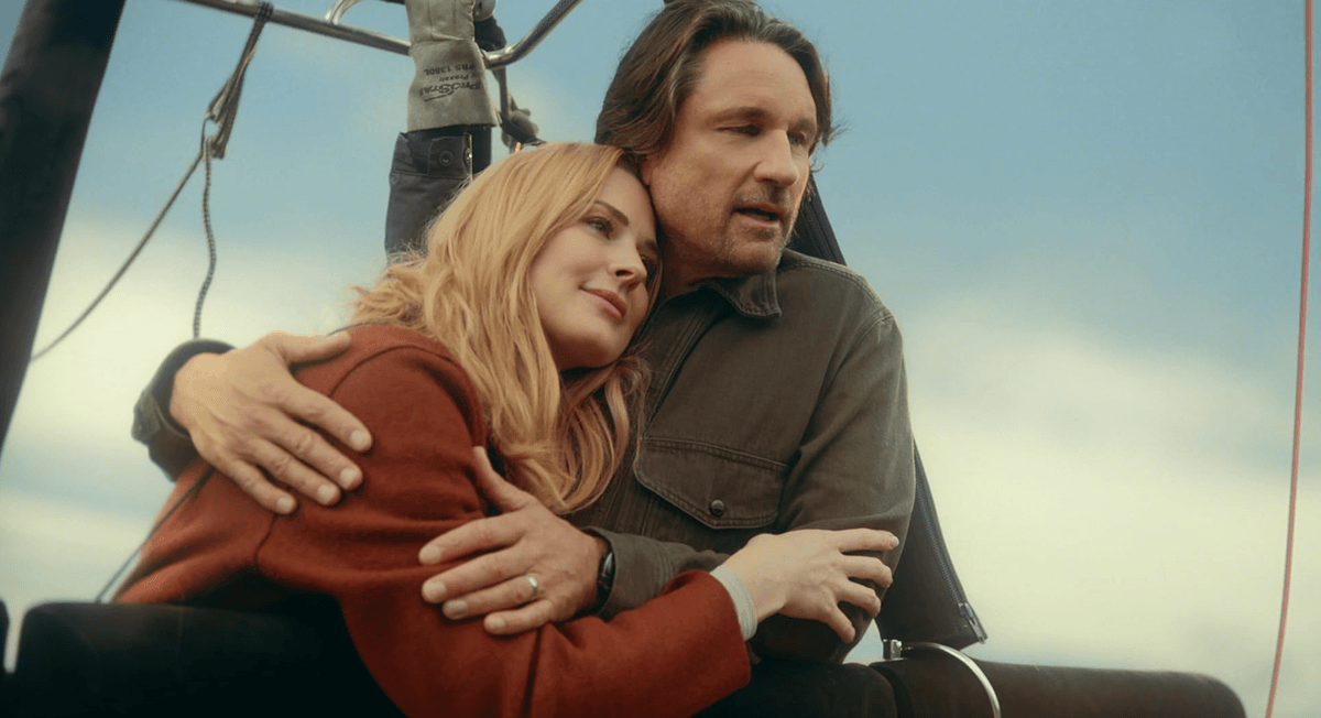 Couple embracing in a hot air balloon basket against a clear sky backdrop.