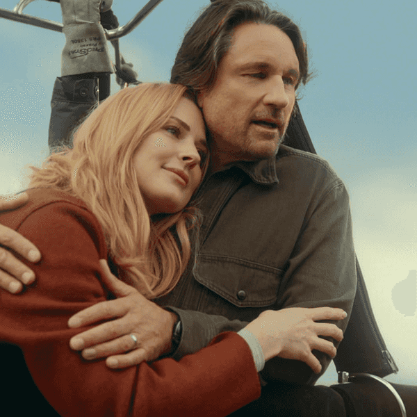 Couple embracing in a hot air balloon basket against a clear sky backdrop.