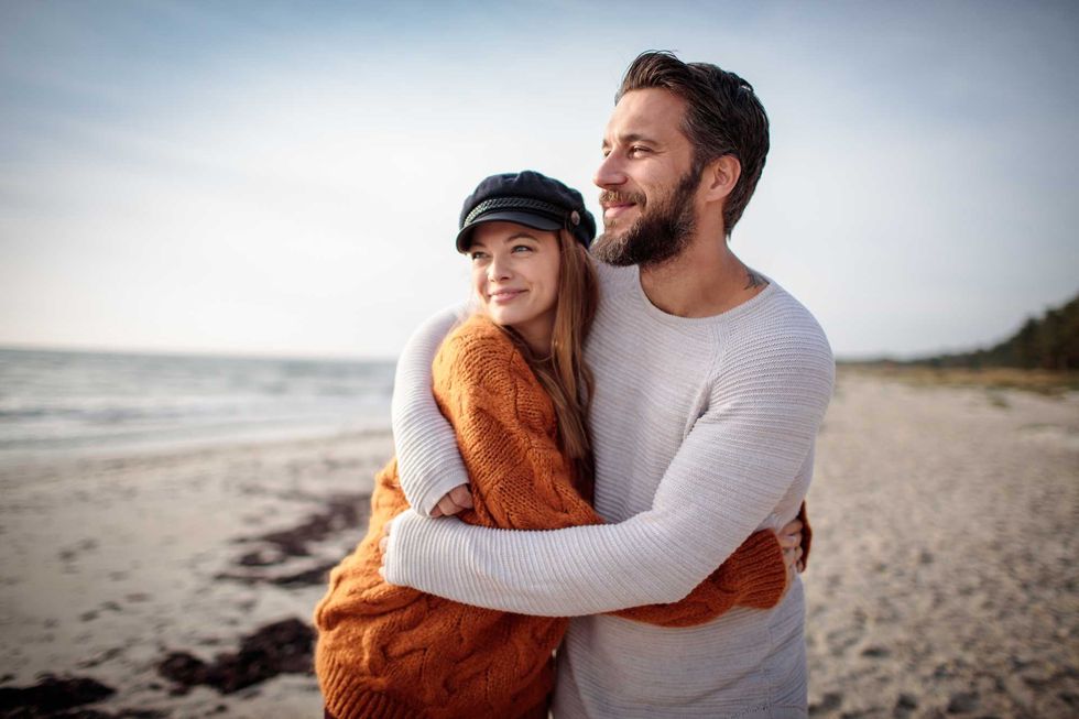 Couple embracing on a beach with a serene ocean view in the background.