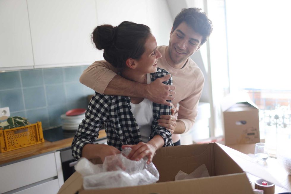 Couple happily unpacking a box in a bright kitchen.