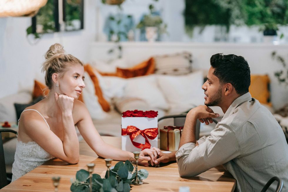 Couple holding hands across a table, with flowers and gifts nearby.