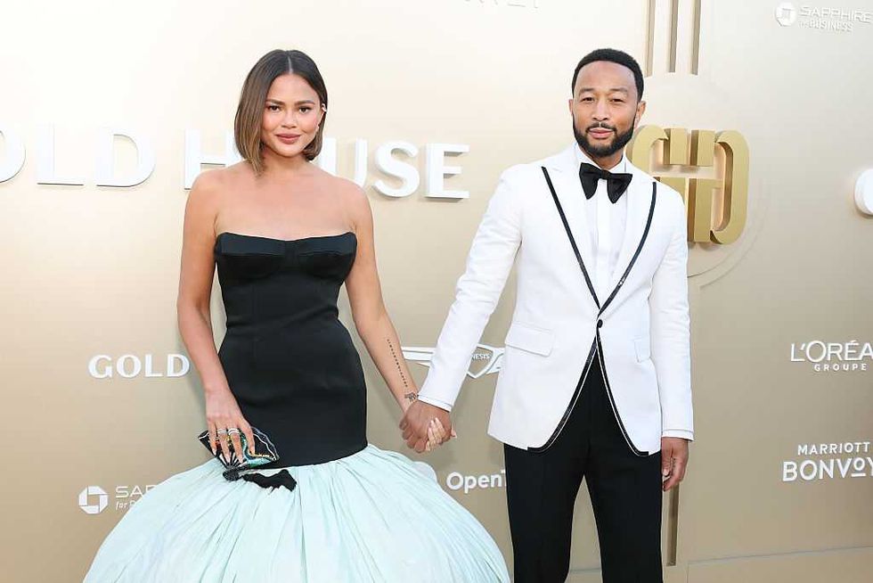 Couple holding hands, woman in gown, man in tuxedo, posing at an event.