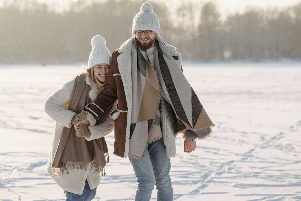 Couple in winter clothing walking and laughing on a snowy field.