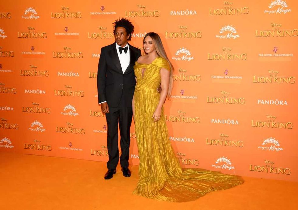 Couple posing on red carpet at "The Lion King" event; vibrant orange backdrop.