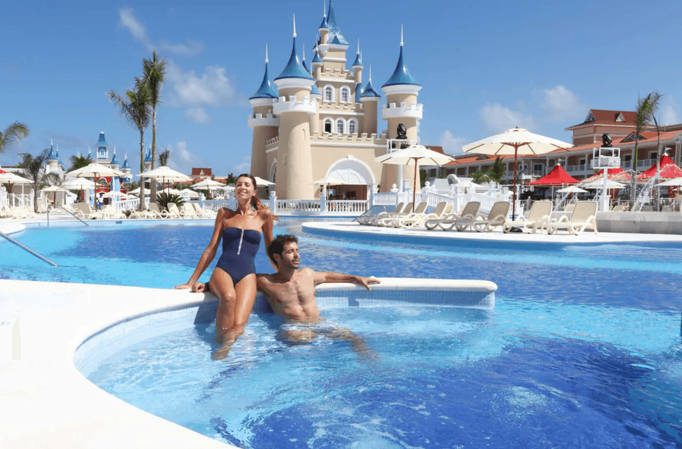 Couple relaxes in a resort pool with a castle-like building in the background.