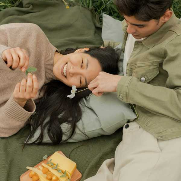 Couple relaxing on a picnic blanket, smiling with snacks and flowers.