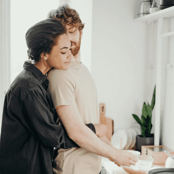 Couple shares a tender embrace while cooking in a bright kitchen.