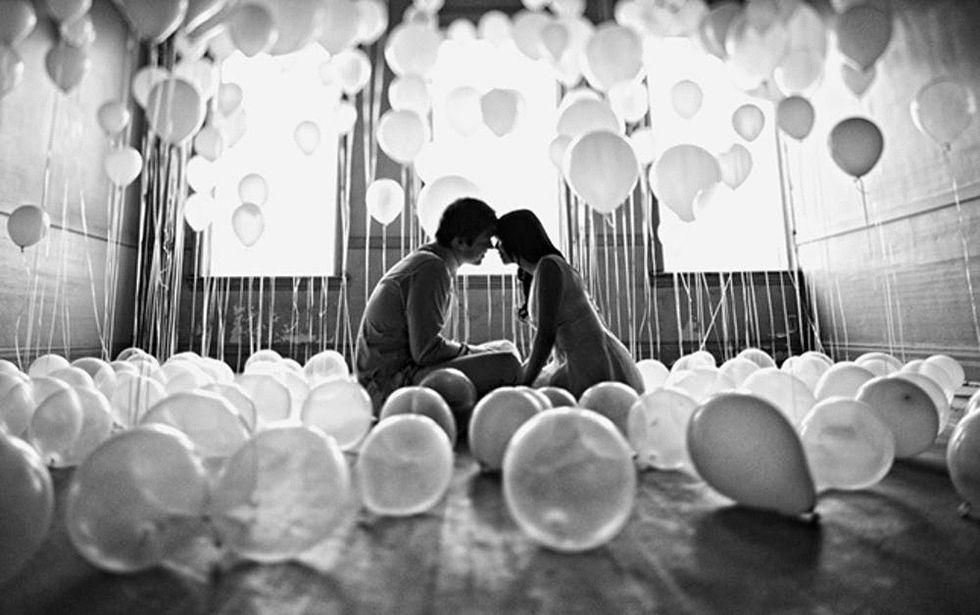 couple sits in a room full of balloons in black and white portrait