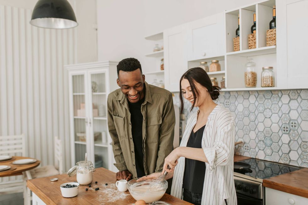 Couple smiling and baking together in a modern kitchen.